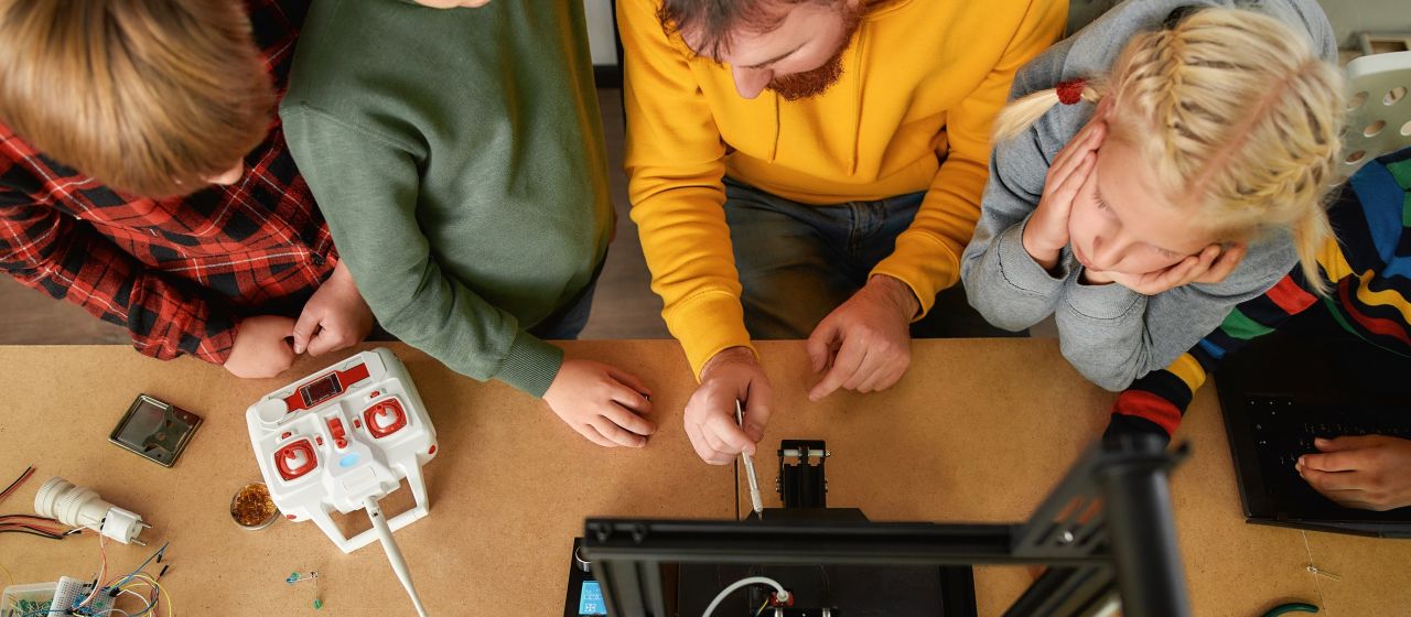 Erwachsener zeigt einem Mädchen und zwei Jungs eine technische Installation